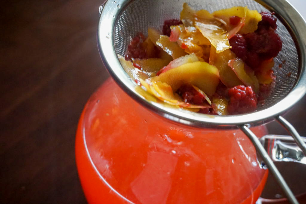 straining the lemon peels and raspberries