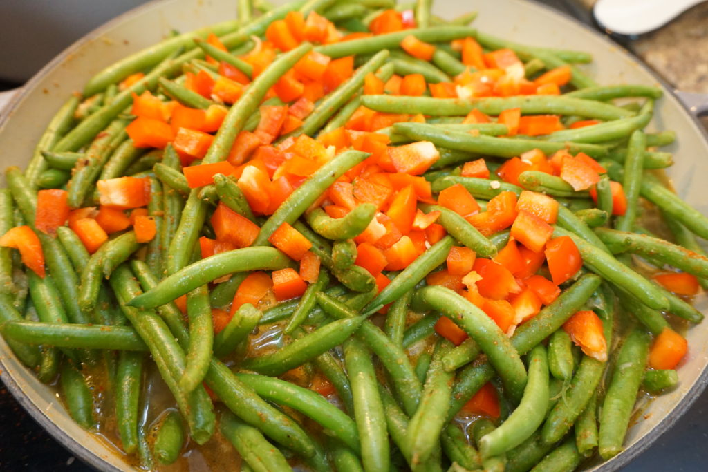 Cooking green beans with onions, red bell peppers, and chicken stock. 