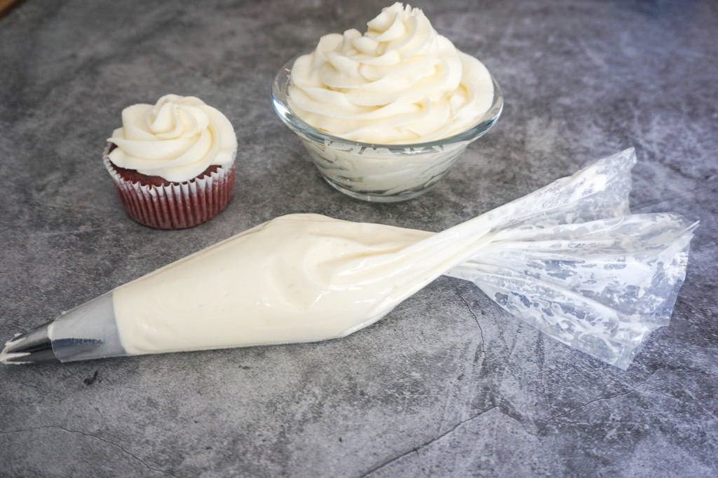 Image of the cream cheese frosting with piping bag and a frosted red velvet cupcake