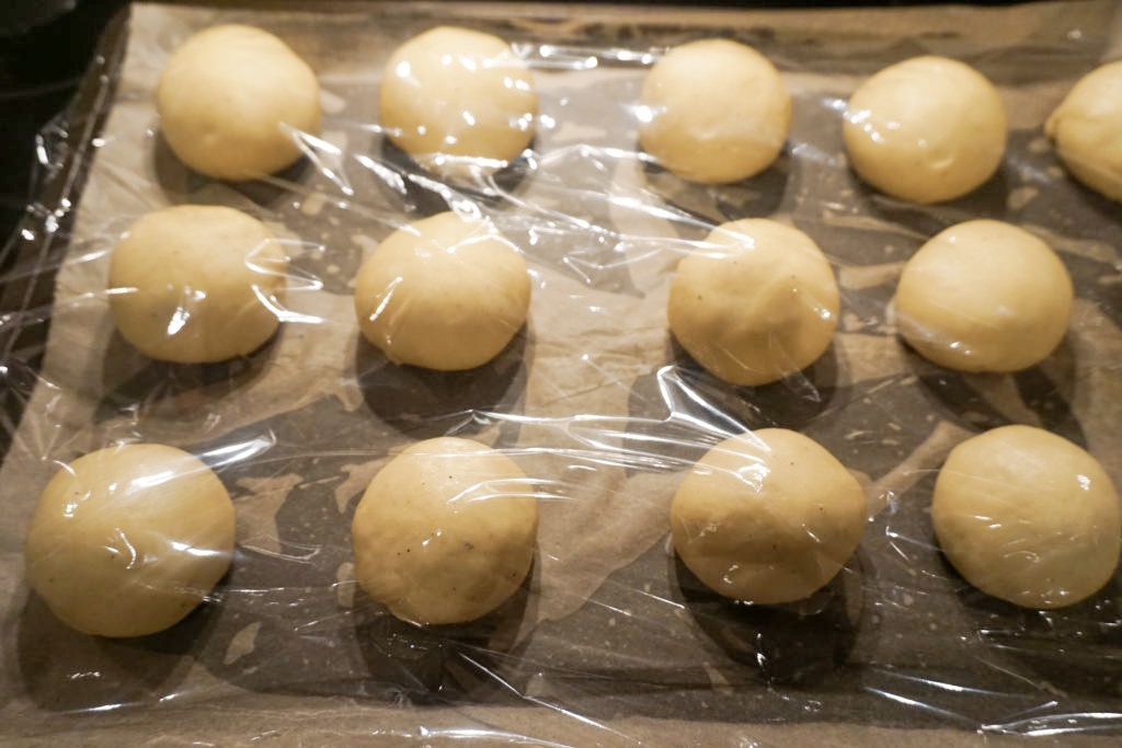 Plastic wrap lightly covering the brioche dinner rolls as they proof