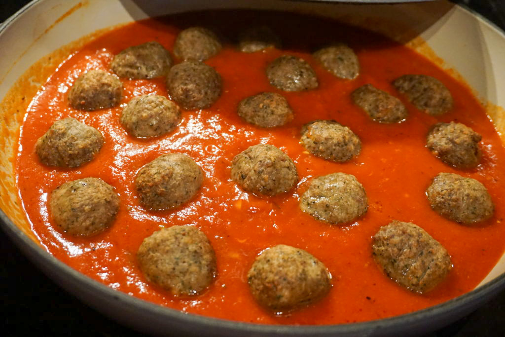 placing the cooked meatballs into the tomato sauce 