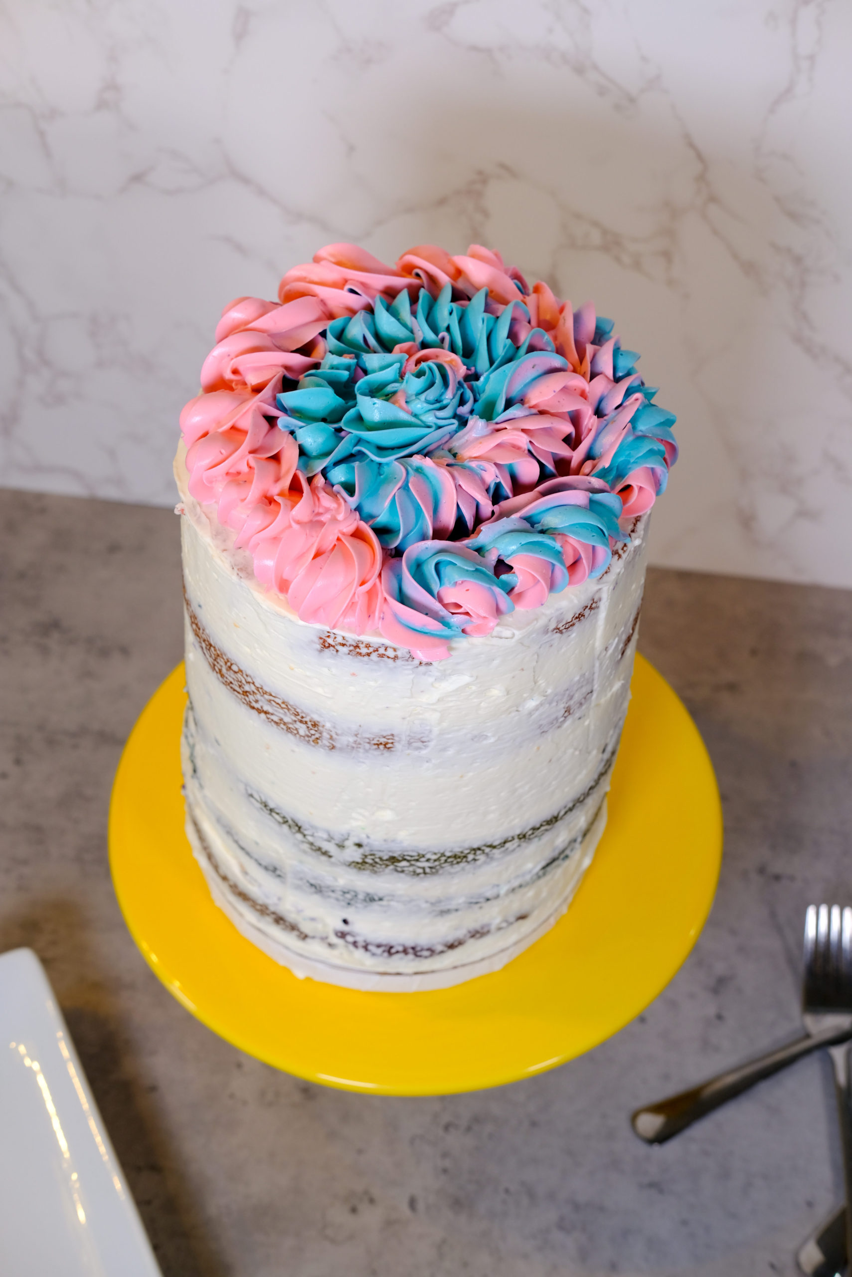 the uncut cake on a yellow cake stand with forks and plates