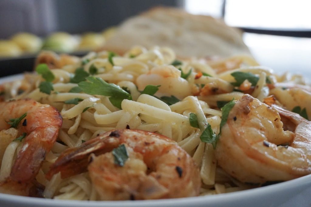 Close up of shrimp scampi with linguine pasta and warm bread.