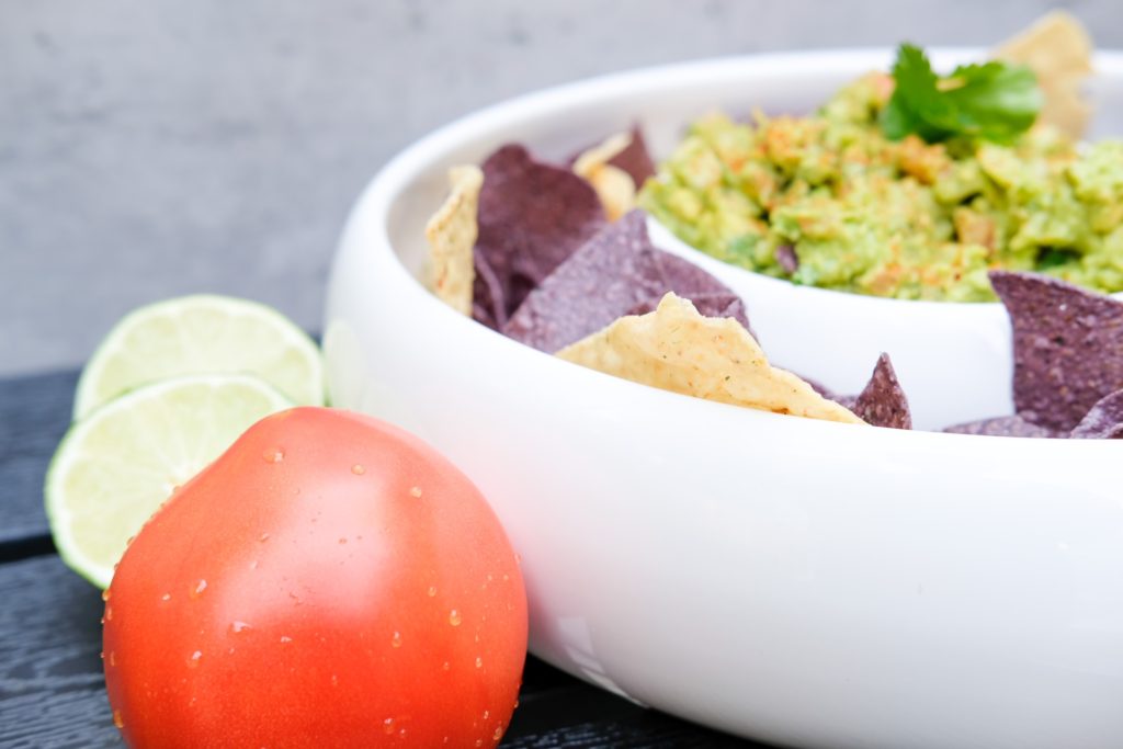 guacamole and chips with a sliced lime and wet tomato 